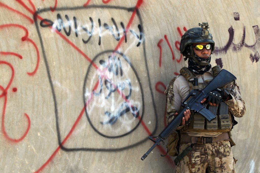 An Iraqi soldier stands next to a wall with a red cross above a slogan of the Islamic State (IS) group, on September 4, 2016 in the city of Fallujah.  Iraq's security forces have for months been battling IS fighters in Anbar province, notching up key victories in provincial Ramadi and jihadist bastion Fallujah earlier this year.  / AFP PHOTO / AHMAD AL-RUBAYE