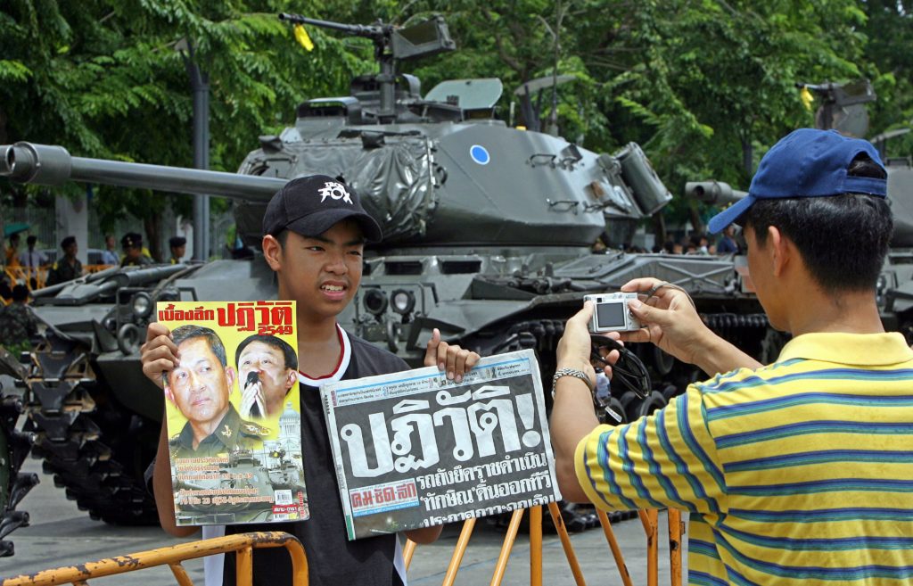 A Thai student (L) poses for a picture while holding a magazine with the pictures of Thai coup leader General Sonthi Boonyaratglin (L) and ousted premier Thaksin Shinawatra (2nd L) in front of tanks at the Royal Plaza in Bangkok, 01 October 2006. Former Thai army chief General Surayud Chulanont has agreed to become the new prime minister in a military-backed government, the leader of last week's coup said 01 October. AFP PHOTO/ Saeed KHAN / AFP PHOTO / SAEED KHAN