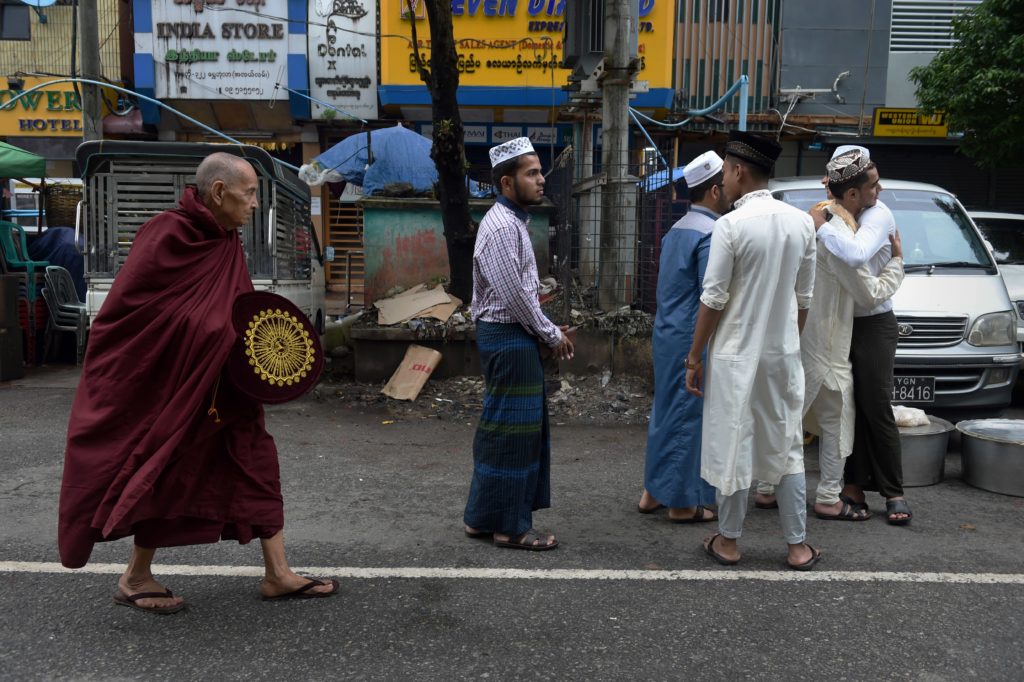 A Buddhist monk (L) walks by Myanmar Muslims (R) greeting one another outside the Narsapuri mosque to mark Eid al-Fitr in Yangon on July 7, 2016 as the country's Muslims celebrate the end of the Islamic holy fasting month of Ramadan. / AFP PHOTO / ROMEO GACAD