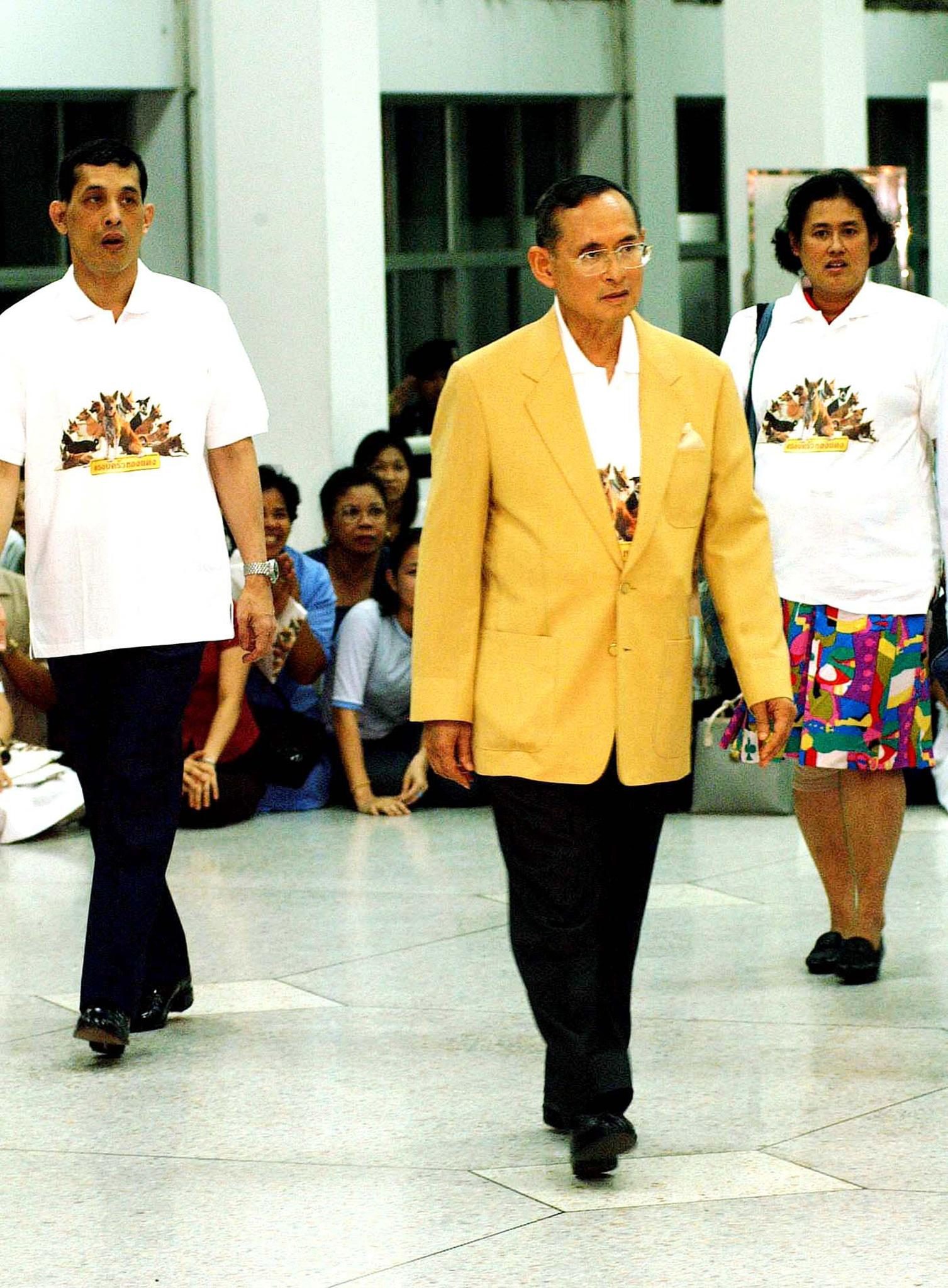 Thailand's King Bhumibol Adulyadej (C) leaves Siriraj Hospital 07 February 2002, flanked by Prince Maha Vajiralongkorn (L) and Princess Maha Chakri Sirindorn, after successfully undergoing prostrate surgery.  The three Royals wore t-shirts printed with a photo, taken by the King himself, of Thongdaeng, the King's dog, and the dog's "family."  The Royal Household has been selling the t-shirt to raise funds for the Bangkok Animal Hosipital.   Thailand's hottest new fashion item -- a T-shirt featuring a stray dog adopted by much-loved King Bhumibol Adulyadej -- has leapt off the shelves after the monarch was pictured wearing one.   AFP PHOTO / AFP PHOTO / STR