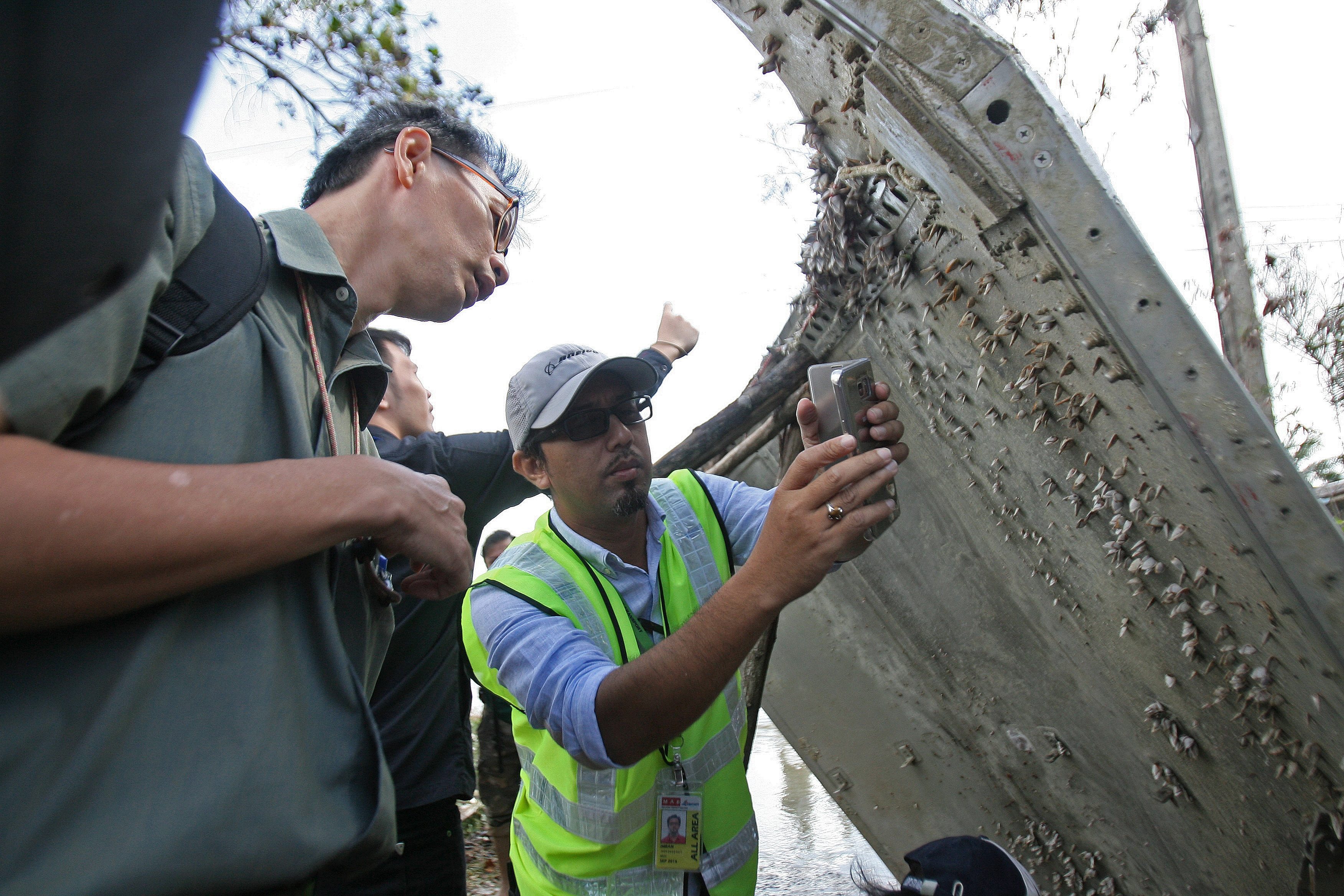 A Malaysian official (C) takes pictures of a piece of suspected aircraft debris after it was found by fishermen on January 23, at a beach in the southern province of Nakhon Si Thammarat on January 25, 2016. Thailand's air force said it would bring a piece of suspected aircraft debris - a metal panel measuring two metres (6.6 feet) by three metres - found on the southeast coast to Bangkok, amid media speculation it may belong to missing Malaysia Airlines Flight MH370. AFP PHOTO / TUWAEDANIYA MERINGING / AFP PHOTO / Tuwaedaniya MERINGING